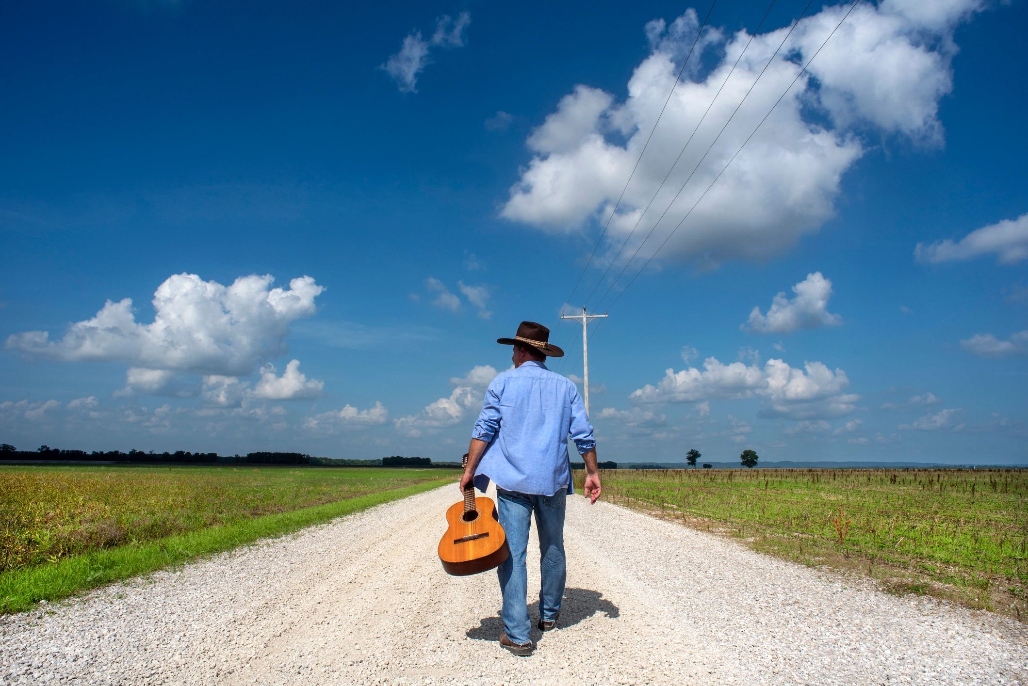 Musician walking with guitar on country road